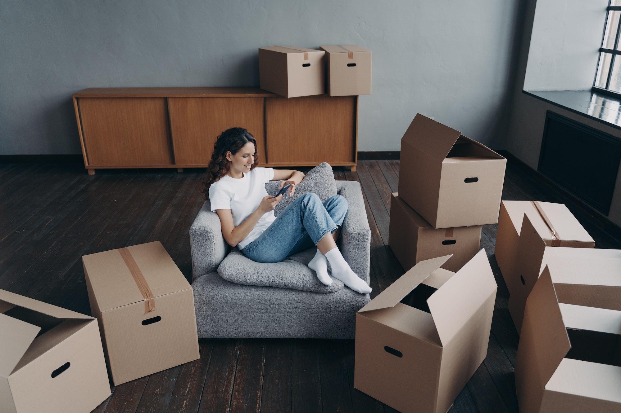 woman-using-phone-purchases-furniture-chooses-relocation-service-to-move-packed-things-to-new-home