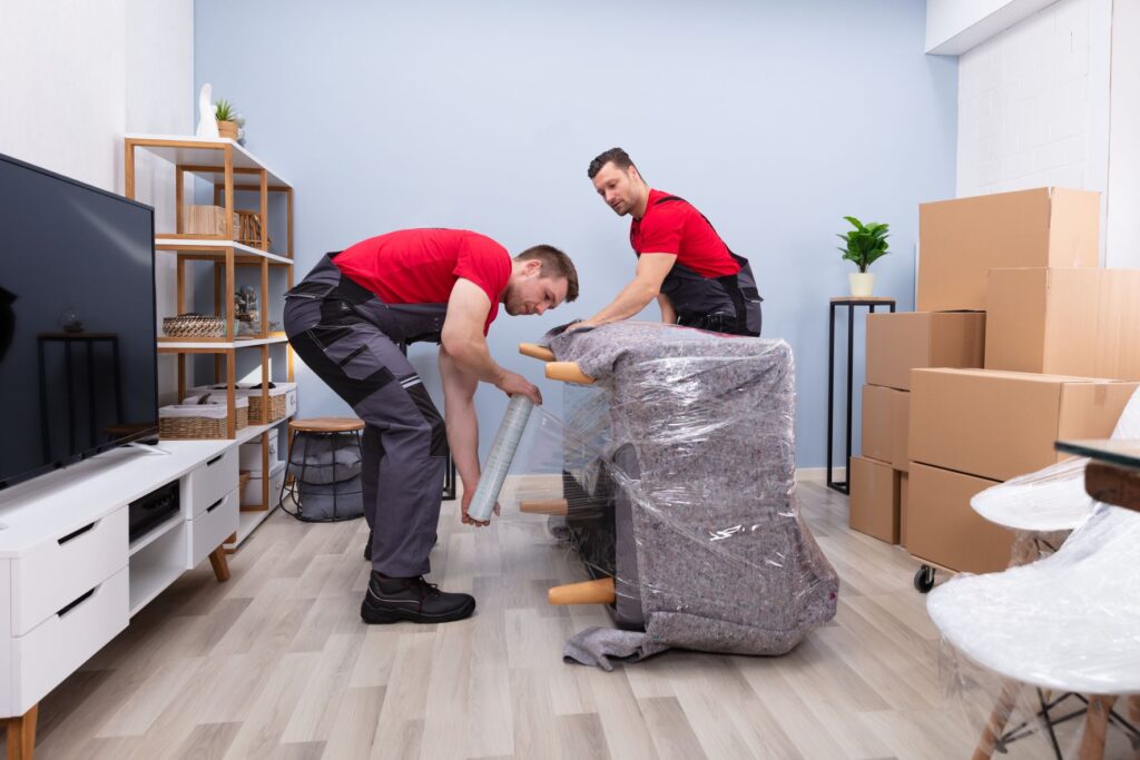 Two movers wrapping furniture for relocation