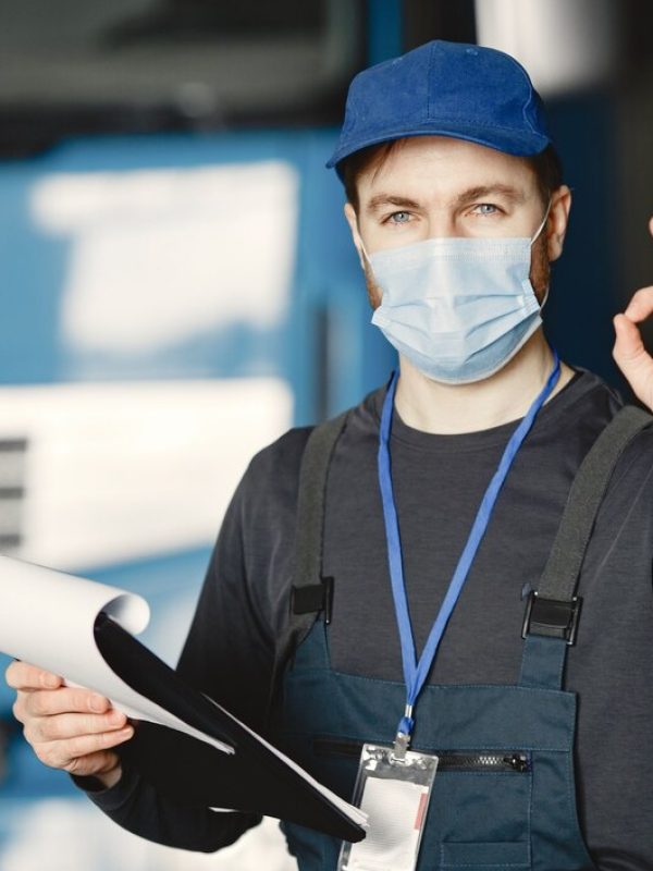 delivery-worker-in-blue-uniform-and-mask-holding-documents-showing-ok-hand-gesture
