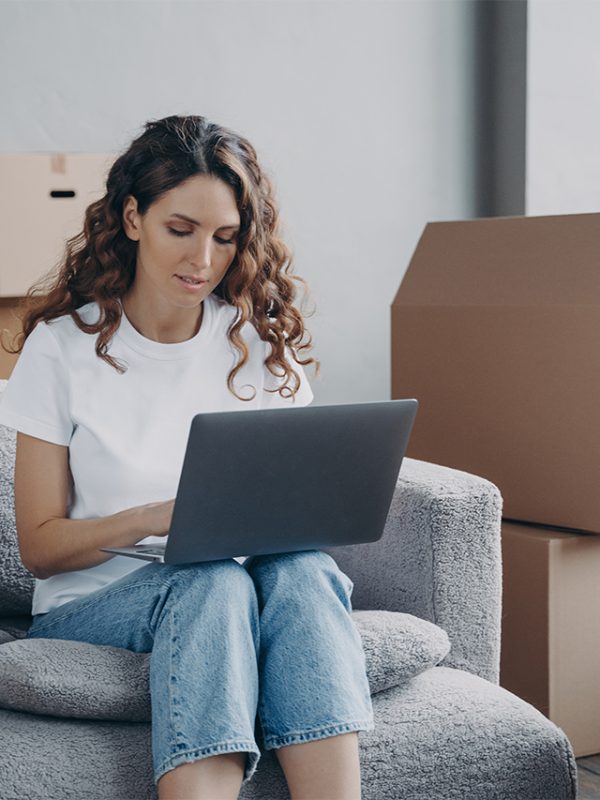 woman-working-on-a-laptop-in-a-room-with-moving-boxes-in-the-background