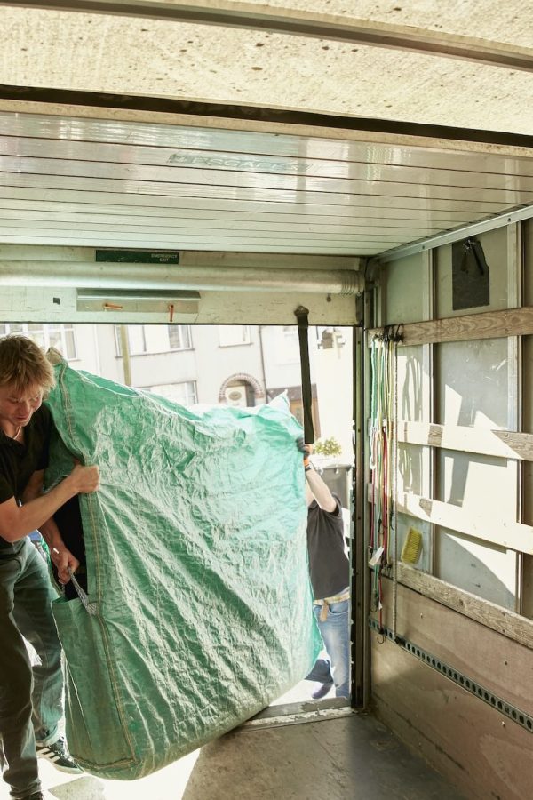 Removals business. A man lifting an item of furniture covered in green plastic into a removals van.