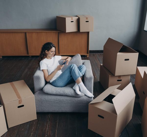 Woman using phone, purchases furniture, chooses relocation service to move packed things to new home