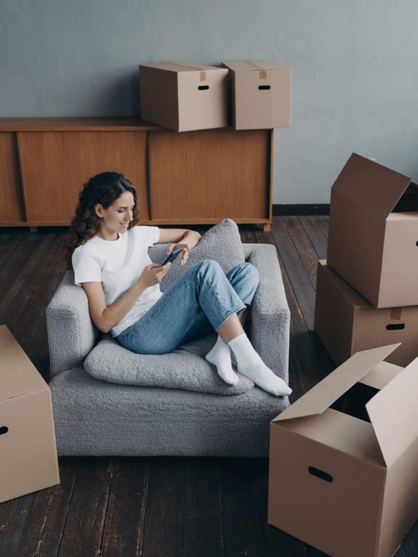 Woman using phone, purchases furniture, chooses relocation service to move packed things to new home